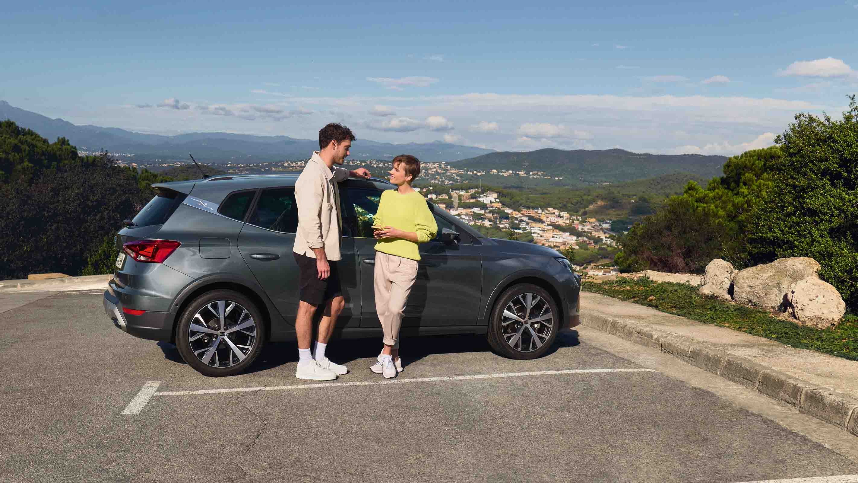 Casal ao lado do SEAT Arona, SUV compacto com design urbano e estilo jovem, ideal para aventuras a dois.