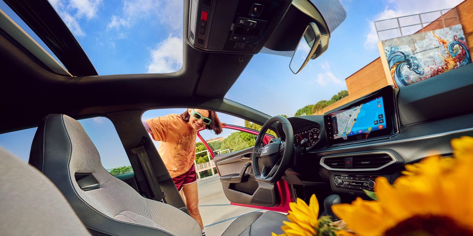Vista do interior do SEAT Ibiza, com um painel de instrumentos moderno, ecrã tátil e teto de abrir, com um ramo de girassóis no banco da frente. 