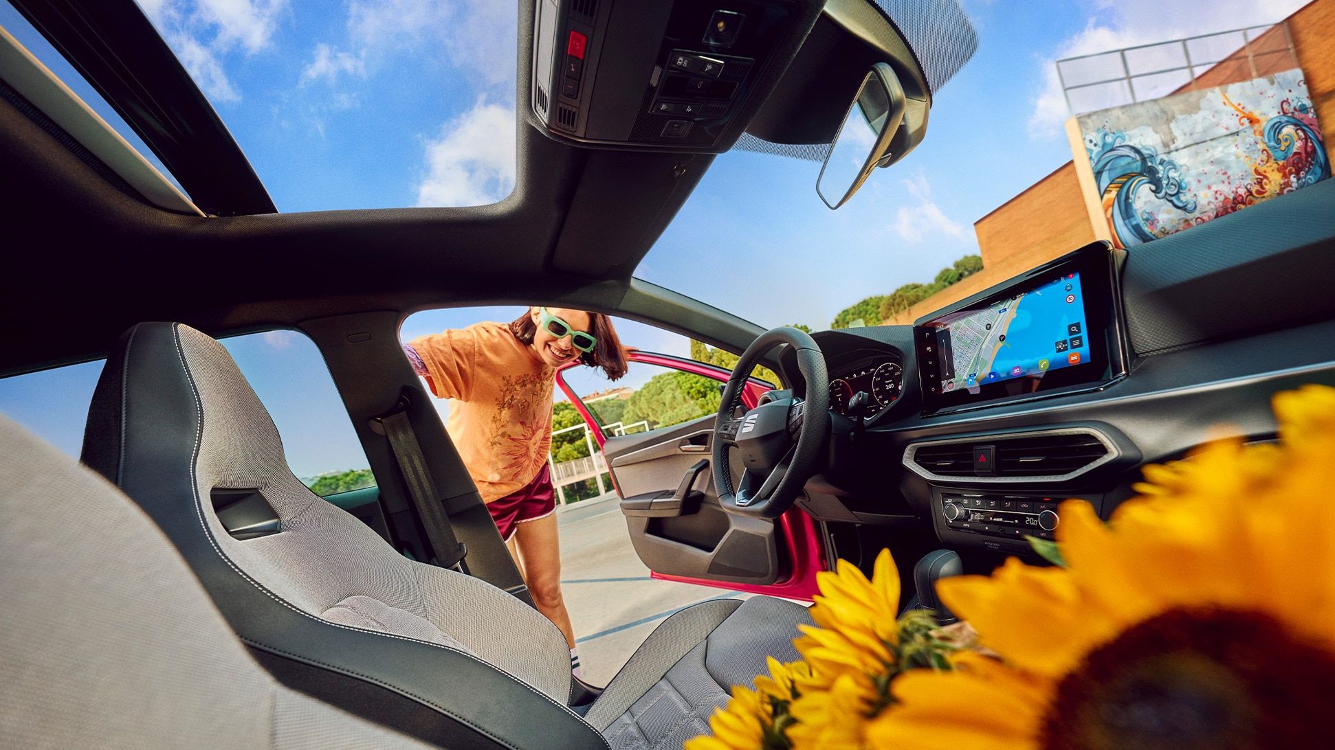 Vista do interior do SEAT Ibiza, com um painel de instrumentos moderno, ecrã tátil e teto de abrir, com um ramo de girassóis no banco da frente. 