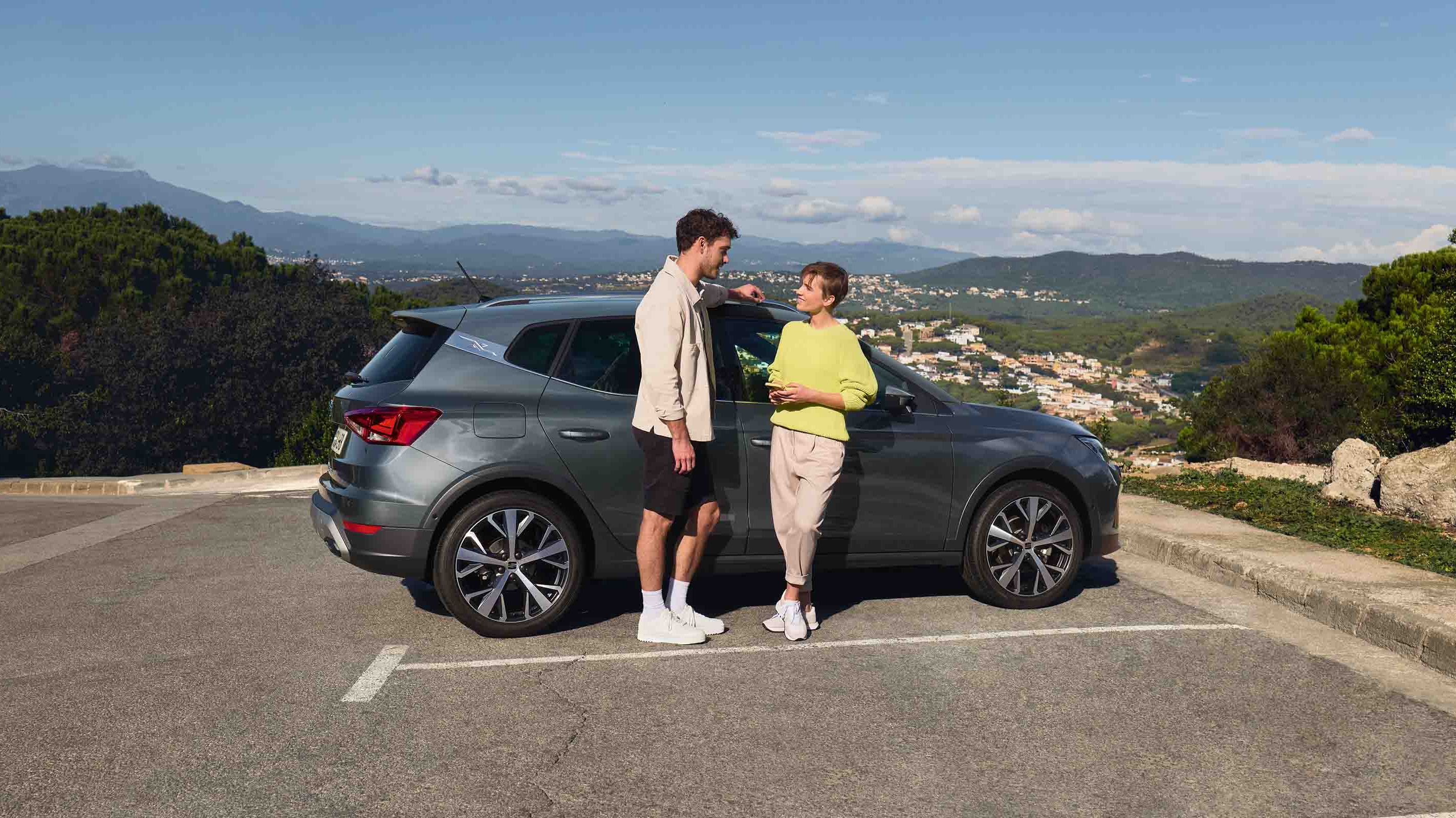 Casal ao lado do SEAT Arona, SUV compacto com design urbano e estilo jovem, ideal para aventuras a dois.