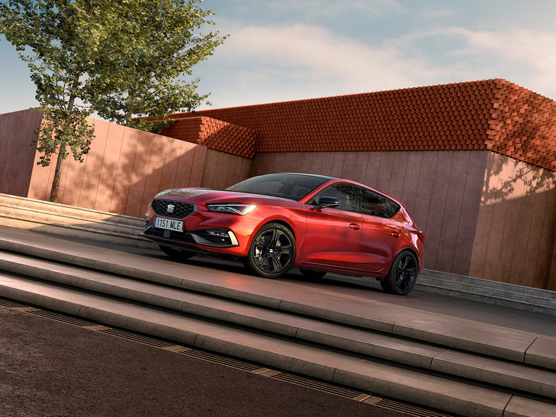 Capas dos espelhos retrovisores pretos brilhantes para o SEAT Leon FR, em contraste com a carroçaria vermelha, vista lateral com fundo de cimento.