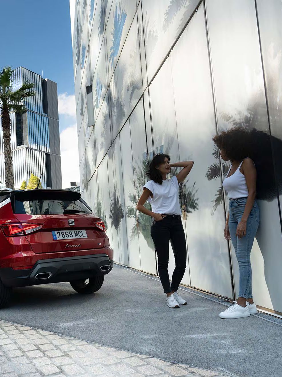 Duas mulheres a conversar e a rir juntas na rua, ao lado de um SEAT Arona na cor vermelho Desire.