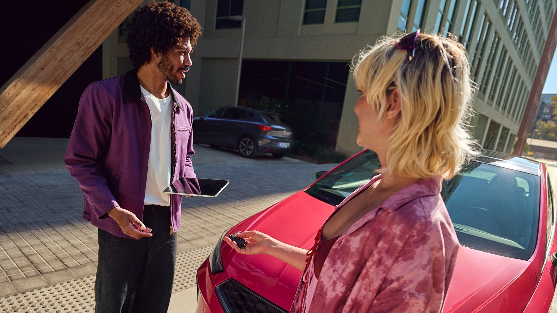 Duas pessoas em pé junto a um SEAT Ibiza vermelho, num ambiente urbano, a segurar chaves do carro e um tablet.