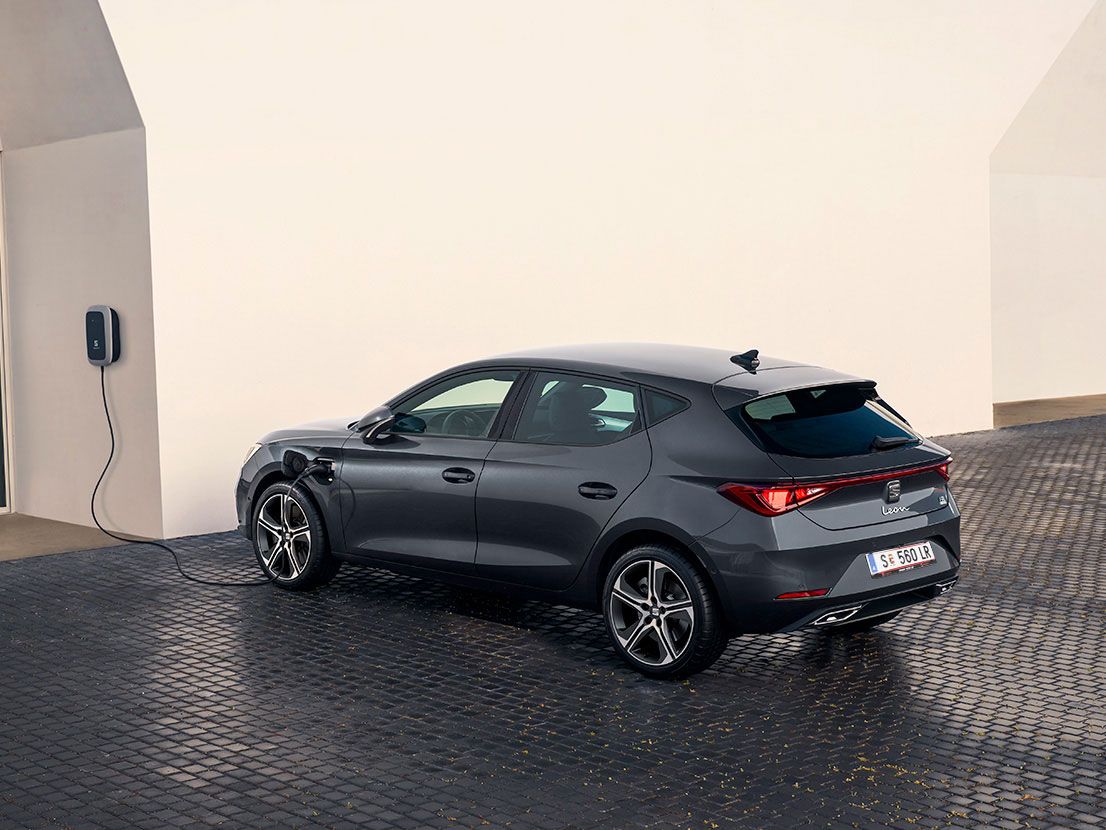 SEAT Leon Hatchback 2025 híbrido plug-in elétrico, estacionado e a carregar no exterior, com jantes de liga leve em raios, iluminação ambiente interior e bancos dianteiros aquecidos para máximo conforto.
