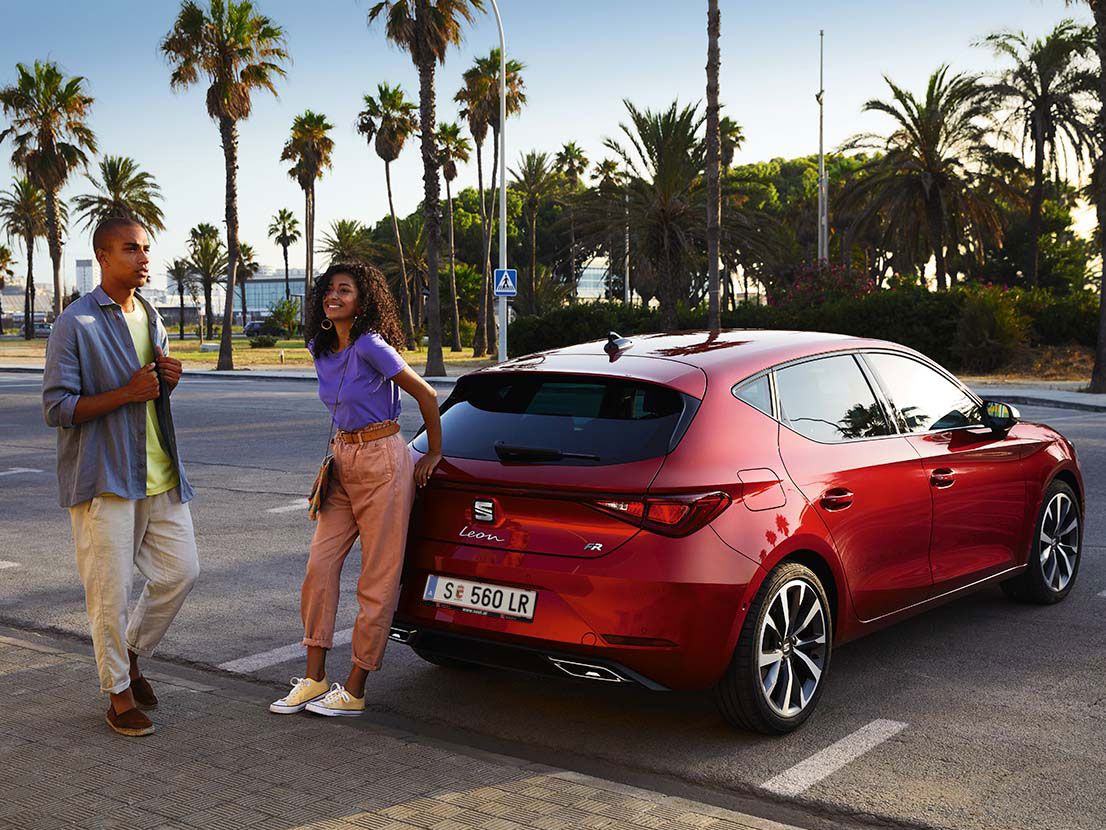 Casal a andar junto ao SEAT Leon vermelho Desire 