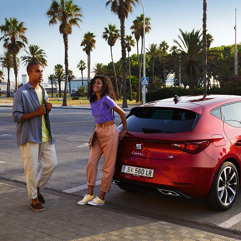 Casal a andar junto ao SEAT Leon vermelho Desire 