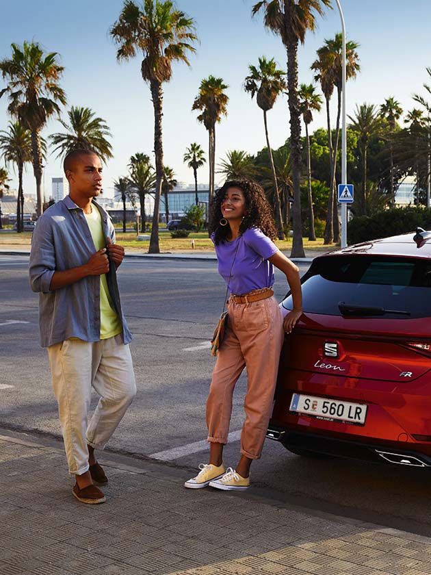 Casal a andar junto ao SEAT Leon vermelho Desire 