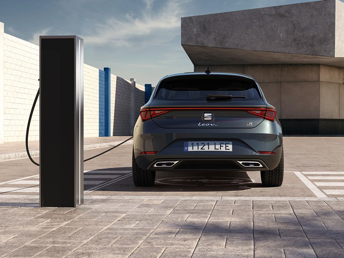 Vista traseira do Seat Leon FR automático a carregar numa estação — o novo hatchback de 2025 em cinzento magnético, equipado com sensores de estacionamento traseiros e luzes LED dianteiras e traseiras.