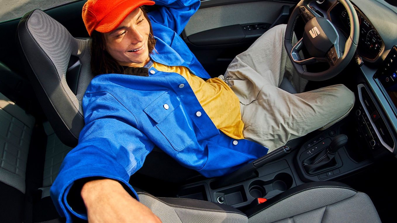 Interior do SEAT Ibiza, com um painel de instrumentos moderno, bancos elegantes e teto de abrir aberto, com uma pessoa reclinada no interior do carro.Interior do SEAT Ibiza, com um painel de instrumentos moderno, bancos elegantes e teto de abrir aberto, com uma pessoa reclinada no interior do carro.