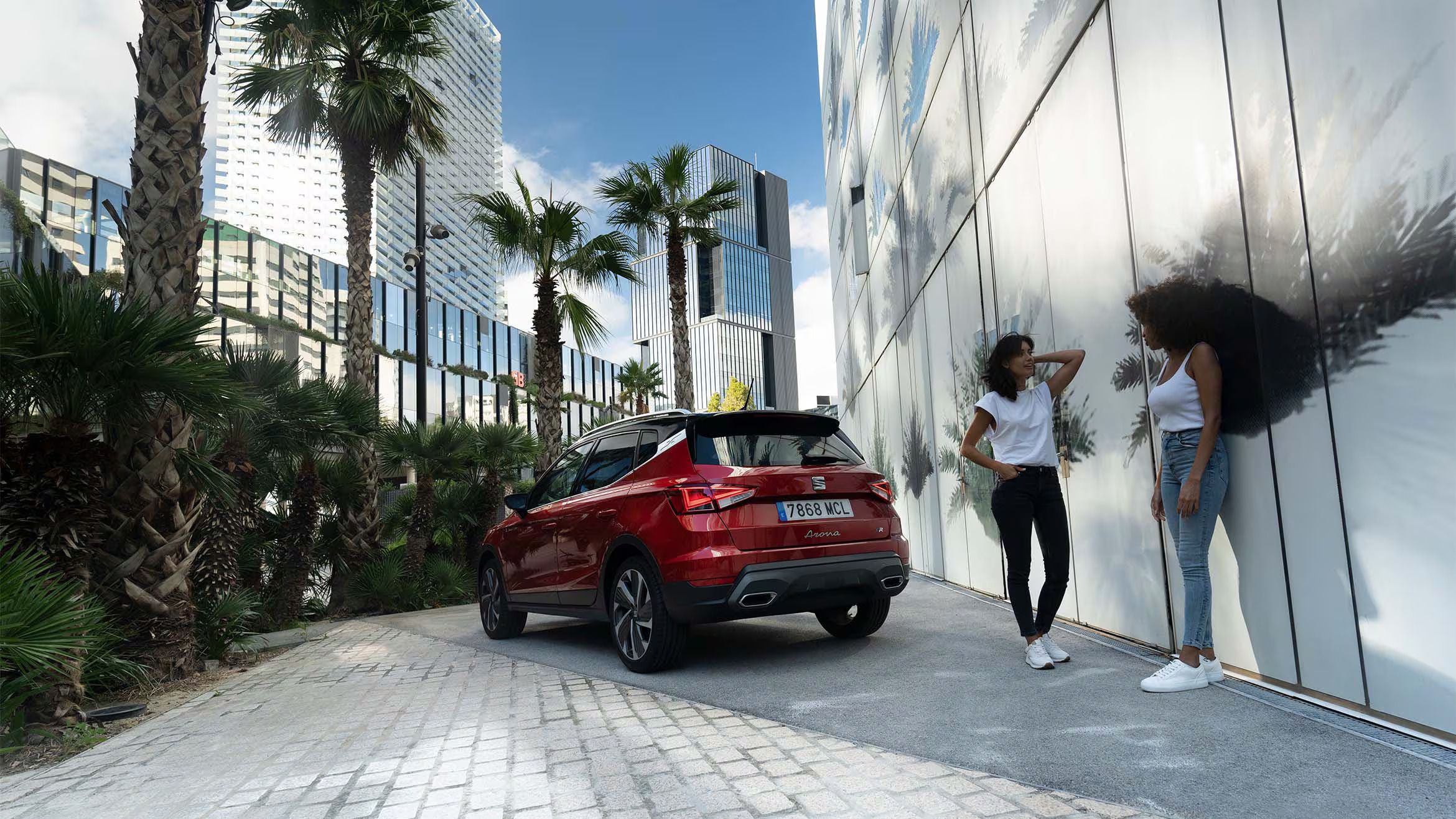 Duas mulheres a conversar e a rir juntas na rua, ao lado de um SEAT Arona na cor vermelho Desire.