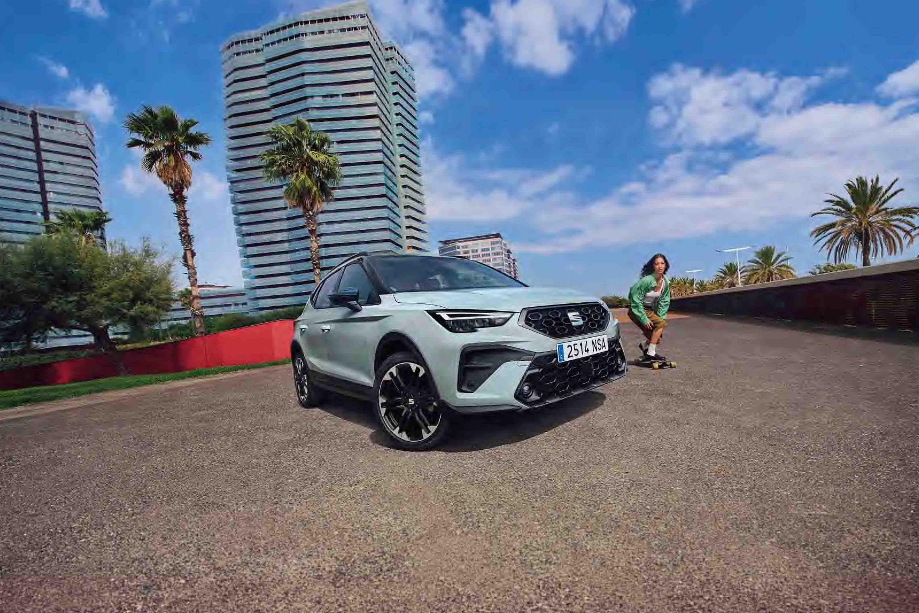 SEAT Arona estacionado numa rua ensolarada com edifícios urbanos modernos e um skater a passar.