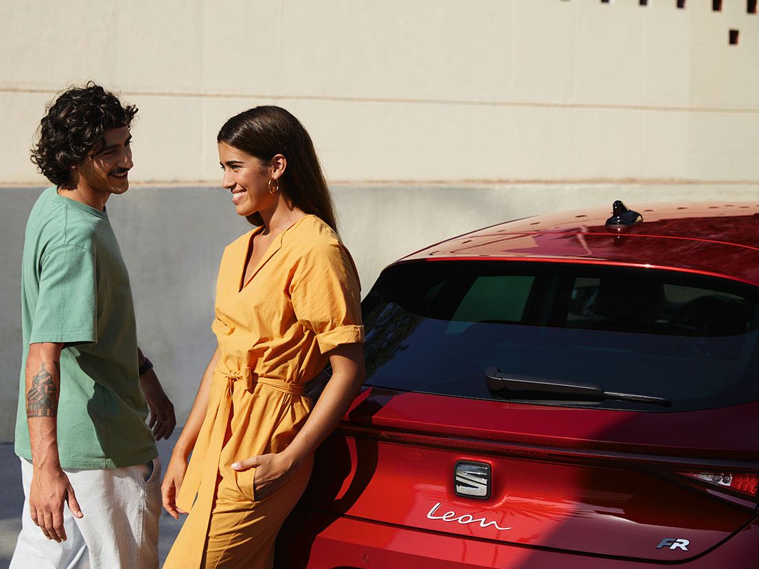 Casal a conversar junto SEAT Leon na cor Vermelho Desire no inverno